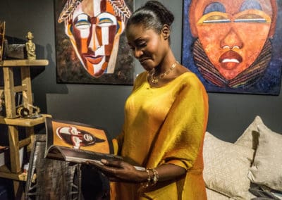 Une dame africaine parcourt le livre sur les masques devant les peintures de Fatoumata Fathy Sidibé.